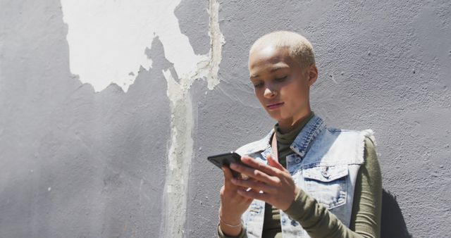 Biracial woman leaning on wall and using smartphone, copy space. Street style, modern urban lifestyle and communication.