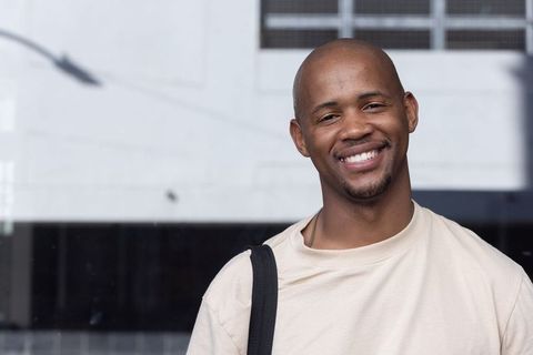 African american man smiling with shoulder bag strap, minimalist urban reflective glass backdrop