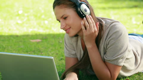 Woman Relaxing in Park Listening to Music on Laptop
