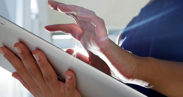 Showcases a businesswoman's hands using a digital tablet with sunlight streaming in. Perfect for business, technology, productivity, or remote work themes. Ideal for advertising software, apps, modern office settings, and work-from-home content.