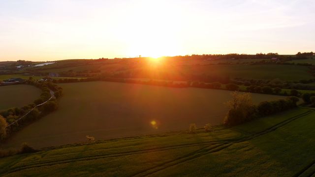 Aerial view of agricultural fields with the setting sun casting vibrant orange light across the landscape. Perfect for use in projects related to agriculture, rural life, nature, tranquility, and scenic beauty.