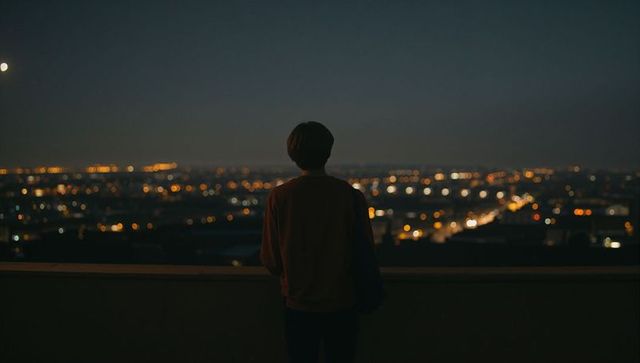 Solitary figure standing on rooftop overlooking city night lights and distant skyline