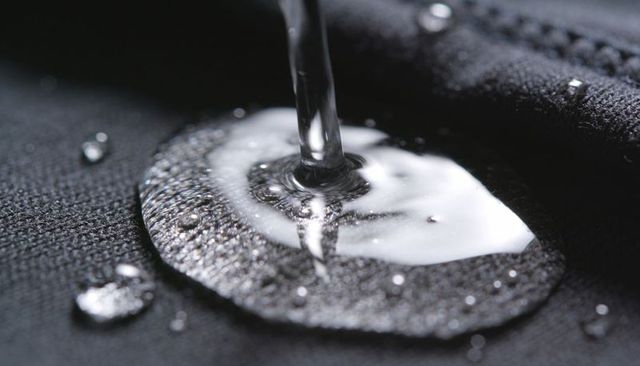 Pouring water beading on black woven fabric macro highlighting hydrophobic texture sheen