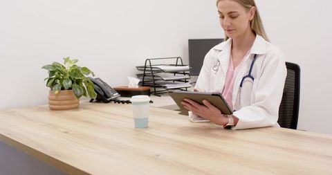 Doctor holding tablet reviewing patient records in modern clinic office with copy space
