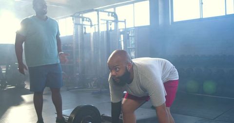 African men performing barbell deadlift with coach spotting in industrial gym workout