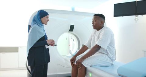 Clinician wearing headscarf consulting patient on ct scan table in bright modern radiology room
