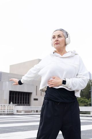Mature woman exercising on urban terrace wearing headphones and smartwatch