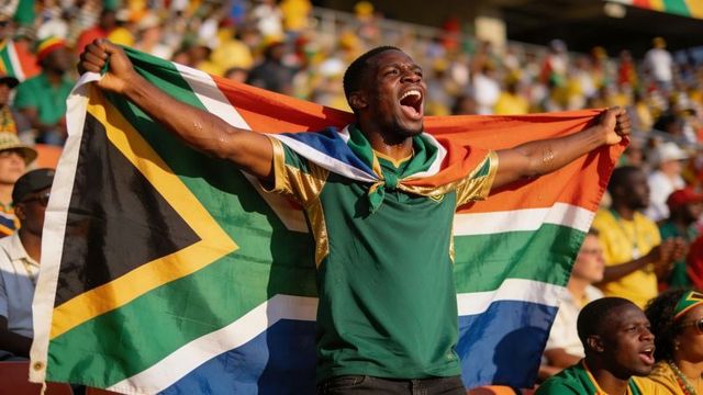 Ecstatic south african football fan cheering and waving large national flag in stadium