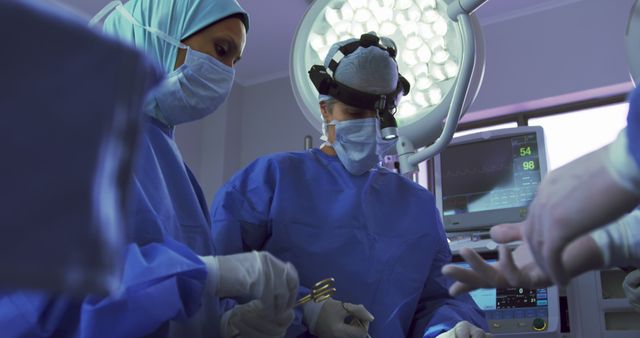 Surgeons are performing surgery in an operating room, dressed in blue surgical gowns and masks. The scene includes advanced medical equipment and a bright surgical light. This image is ideal for healthcare articles, medical textbooks, or hospital promotional materials, showcasing the professionalism and precision of medical procedures.