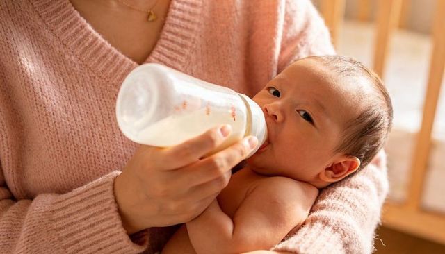 Cradling parent feeding newborn with bottle in cozy nursery, tender bonding moment