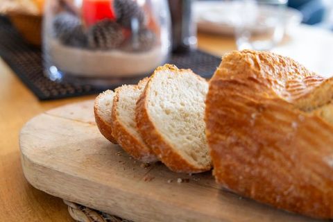 Rustic artisan bread being sliced on wooden board with crumbs and warm kitchen ambiance
