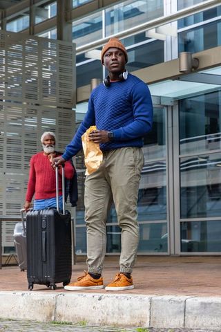 African american traveler wearing beanie and quilted sweater with luggage at transit