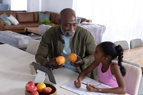 African american grandfather sharing oranges teaching granddaughter nutrition at kitchen table