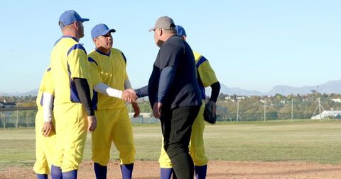 Community baseball team shaking hands with coach on sunlit infield before game