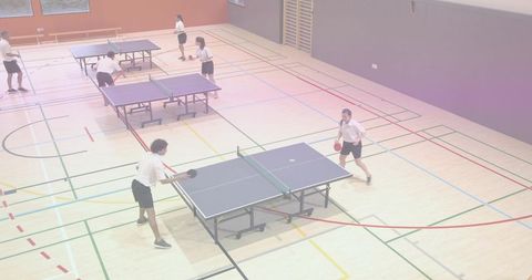 Students playing table tennis in school gym during pe class, practicing rallies and teamwork