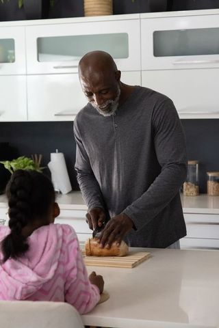 African american father slicing bread at kitchen island as daughter watches