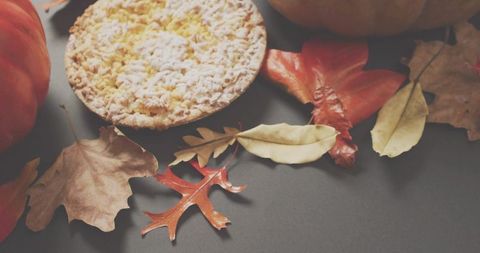 Rustic pumpkin crumb tart sitting among autumn leaves and pumpkins on gray tabletop
