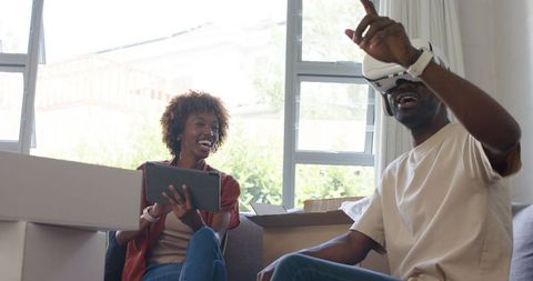 Couple enjoying virtual reality while unpacking in new home, laughing together