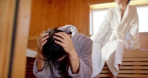 Diverse couple relaxing in sauna, woman comforting man on wooden bench