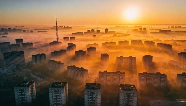 Sun rising over fog-filled residential highrises with radio towers piercing golden morning mist