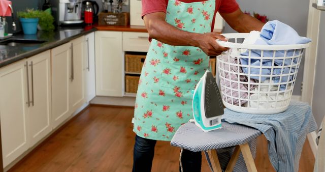Man actively doing laundry and ironing at home, showcasing commitment to household chores. Ideal for articles and advertisements related to housekeeping, domestic responsibilities, and homemaking tips. Use in blogs or social media posts promoting equal sharing of household duties.