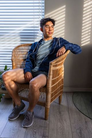 Asian man relaxing in wicker chair by window with blinds casting striped sunlight