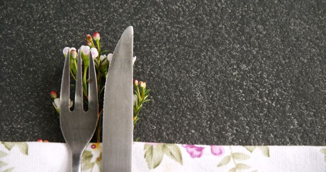 A fork and knife are neatly placed on a floral napkin, with copy space. The arrangement suggests a dining setting, in preparation for a meal or a festive occasion.