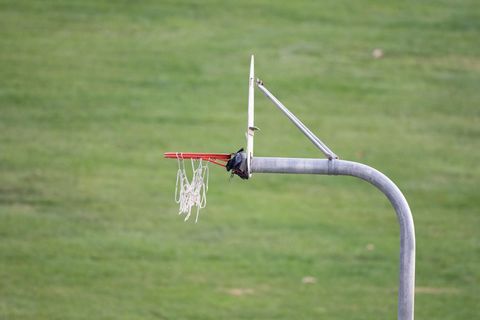 Worn basketball hoop with torn net standing over empty green park field