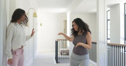 Diverse female friends laughing and gesturing in bright upstairs hallway with brass sconces
