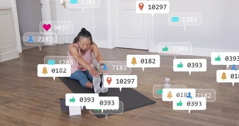 Senior woman stretching on mat at home with social media notifications during online yoga