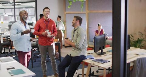 Colleagues Sharing Coffee and Laughing in Modern Open Office Workspace