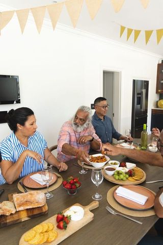 Multigenerational diverse family passing dishes and chatting around modern dining table