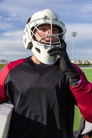 Focused field hockey goalkeeper adjusting helmet on turf