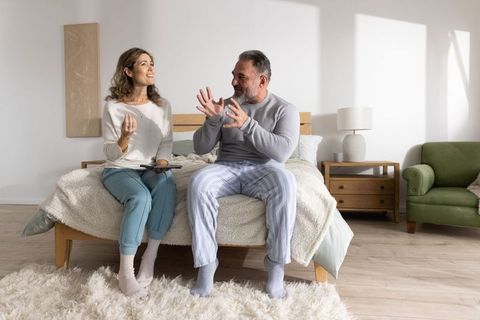 Middle-aged couple chatting and laughing on bed in cozy sunlit minimalist bedroom