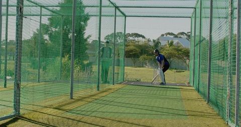 Batter preparing at outdoor cricket practice net with coach observing, sunny training