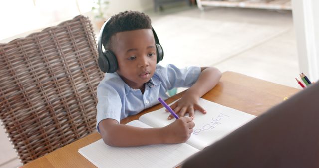 Focused Young Boy Wearing Headphones Writing in Notebook at Table - Download Free Stock Images Pikwizard.com