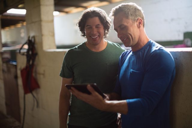 Two male friends using digital tablet in the stable