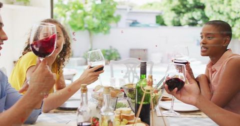 Friends toasting red wine at backyard alfresco dinner party on sunny patio table