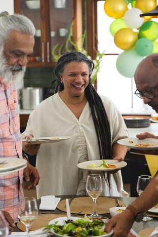 Multigenerational friends gathering around kitchen table laughing and serving food