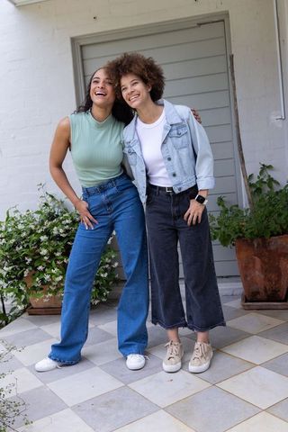 Two african american women laughing and leaning on home porch wearing denim casual fashion