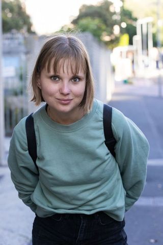 Young woman leaning toward camera wearing green sweatshirt with backpack urban portrait