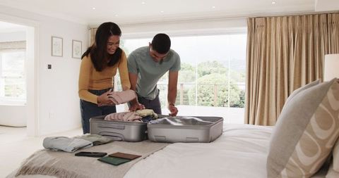 Young Couple Packing Suitcase on Bed for Summer Vacation