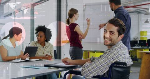 Smiling man in wheelchair taking notes during inclusive team meeting in modern open office
