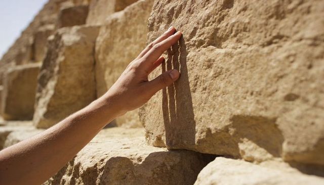 Explorer hand touching sunlit ancient stone blocks in desert ruins casting finger shadow