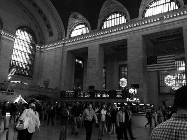 Classic interior shot capturing the hustle and bustle of Grand Central Terminal in black and white. Image highlights impressive architectural features and the crowd moving through the hall. Perfect for use in travel blogs, urban life articles, or pieces on historic landmarks and city transportation.