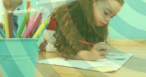 Young girl coloring on wooden floor with colored pencils and turquoise cup, creative play