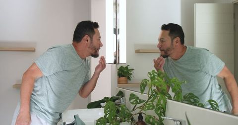 Asian Man Examining Beard in Modern Bathroom Mirror