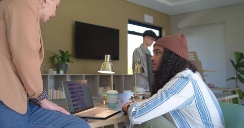 Beanie-wearing teammate collaborating with colleague at sunlit modern coworking desk