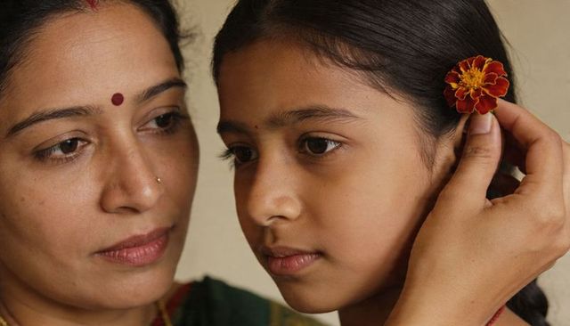 Indian mother tucking marigold into daughter hair closeup portrait of family tradition and bond
