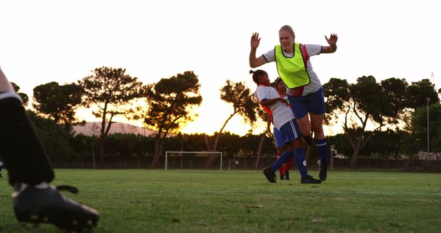 Female soccer players training during sunset on a grassy soccer field. The players are wearing sports gear and showcasing teamwork and athleticism. Ideal for content related to sports, women's athletics, outdoor activities, teamwork, and fitness.